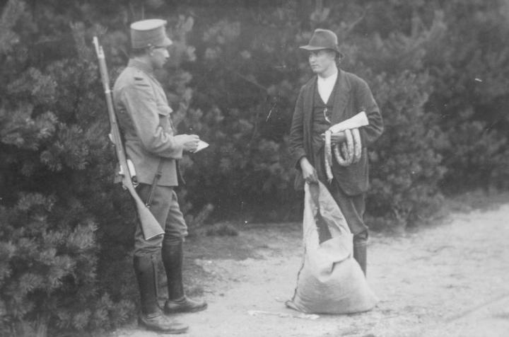 Gestellte Schmuggelszene in schwarz-weiß. Ein Mann mit Gewehr ein anderer Mann mit einem großen Sack stehen sich gegenüber.